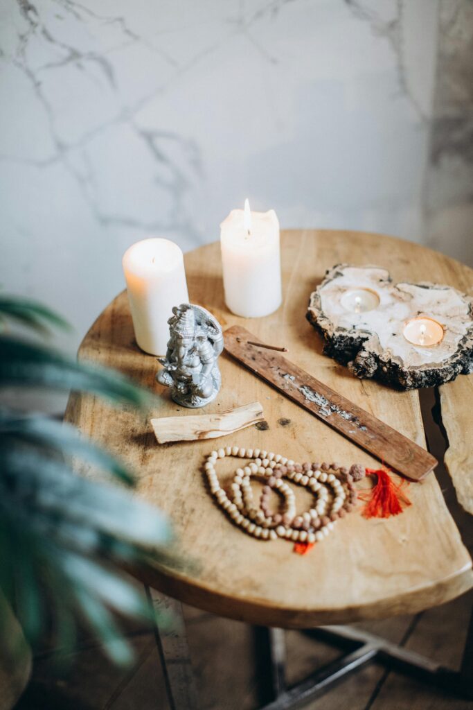 Peaceful still life featuring a Ganesha statue, candles, incense, and prayer beads on a wooden table.