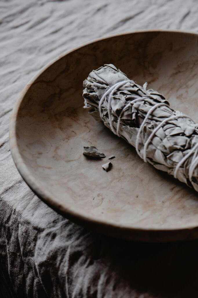 A white sage smudge stick on a rustic wooden plate, ideal for spiritual rituals and cleansing.
